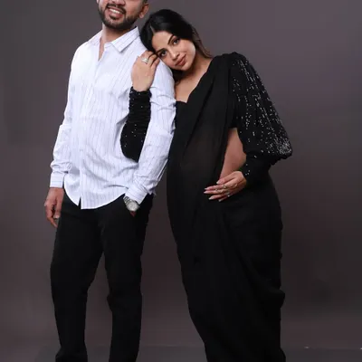 A modern take on a traditional look. The mom-to-be wears a stylish black saree with sequined sleeves, resting her head on her partner's shoulder for a sweet and contemporary couple's portrait.
