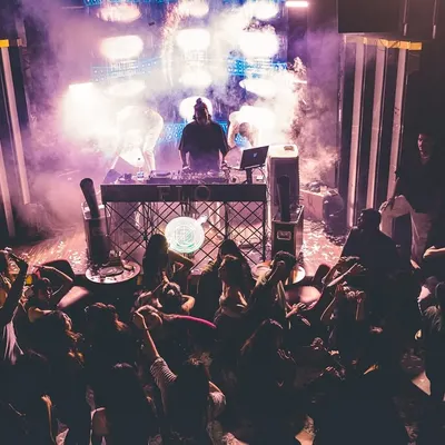 From my perspective behind the console, commanding a packed dance floor under a haze of purple lights and smoke. This is a typical high-energy night where the music takes over.