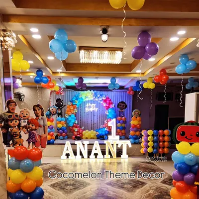 A vibrant Cocomelon theme for Anant's first birthday, filling the entire stage. This setup includes character cutouts, themed balloon columns, a rainbow balloon arch, and large LED letters spelling out the name.