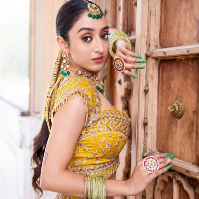 For a Mehendi function, a green-beaded jewellery set is a perfect choice. This model wears a Kundan choker with matching earrings, maang tikka, and statement rings that complement her yellow outfit beautifully.
