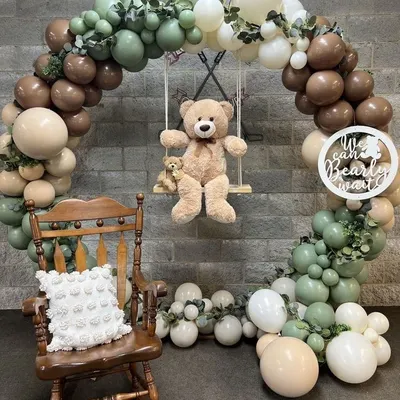 A rustic teddy bear theme with a teddy on a swing inside a balloon arch. The arch uses sage green, beige, and brown balloons, perfect for a "We Can Bearly Wait" baby shower.