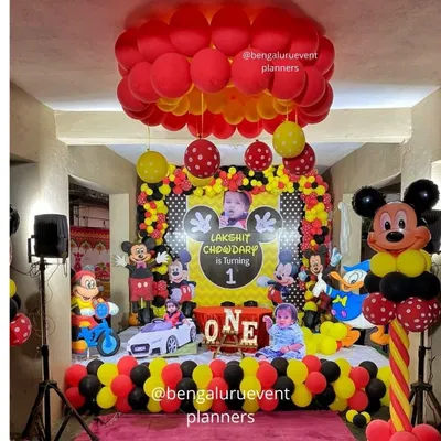 This is a complete Mickey Mouse themed first birthday party I created. The setup includes a personalized backdrop with the child's photo, multiple character cutouts, and coordinated red, yellow, and black balloon decorations for a fun and immersive experience.