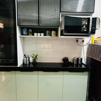 A modern kitchen design featuring serene sage green base cabinets and upper cabinets with trendy fluted glass. The black countertop and dedicated microwave unit complete the contemporary look.