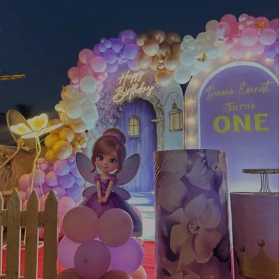 A wide view of our Royal Princess and Butterfly theme, designed for a magical first birthday. The setup includes a custom-printed backdrop with a fairy door, a large balloon arch, themed plinths, and a cute fairy cutout.