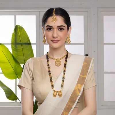 A beautiful shot of a model wearing a traditional gold mangalsutra set. The clean background and soft lighting ensure the focus remains on the jewelry's intricate design and the model's elegant expression.