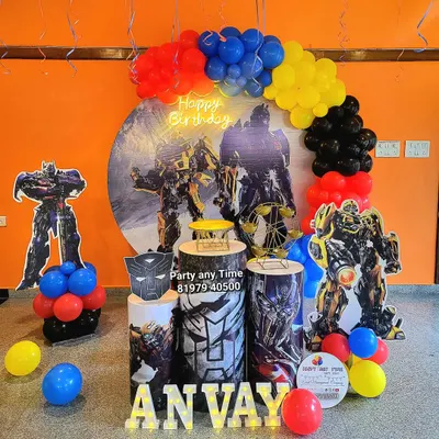 An action-packed Transformers theme for Anvay's birthday. This setup features large character cutouts, a themed backdrop, matching plinths, and a balloon arch in the classic red, blue, yellow, and black colors.