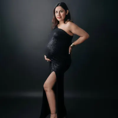 A full-length solo portrait of a mom-to-be looking powerful and elegant in a black one-shoulder sequin gown. This studio shot showcases a glamorous and confident maternity style.