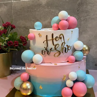 He or She? This two tier gender reveal cake is full of suspense and excitement, decorated with pink, blue, and gold chocolate spheres. It's a fun way to share your big news with family and friends.