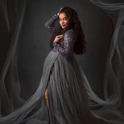 Creating a dreamy, ethereal look with flowing fabrics. This maternity session combines a glamorous sequined gown with soft, sheer drapes for a truly magical portrait against a classic studio backdrop.
