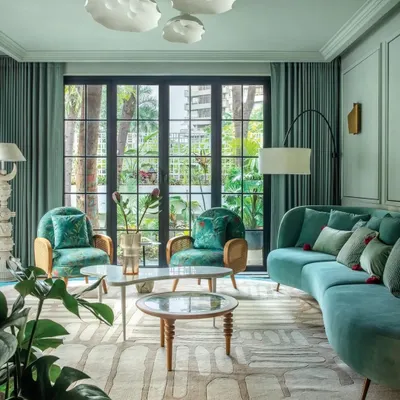 The living room of Summer Haus, a Mumbai bungalow we redesigned for a creative family. The space is filled with color and texture, from the turquoise furniture to the patterned rug, all set against serene green walls and large windows that open to the garden.
