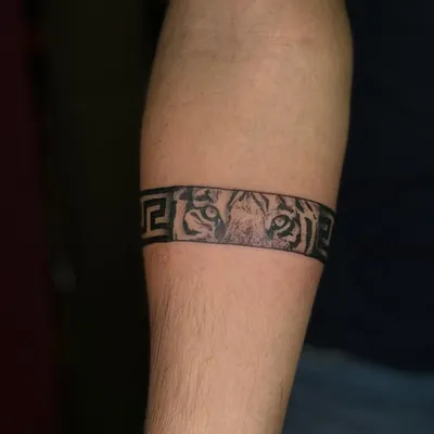 A unique armband tattoo combining a geometric Greek key pattern with the intense eyes of a tiger. This design is both powerful and intricate.