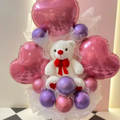 A sweet and romantic teddy bear bouquet. This arrangement features a white teddy bear surrounded by pink and purple balloons and metallic pink heart-shaped foil balloons.