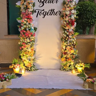 A close-up of the dense floral pillars used for the "Better Together" backdrop. The arrangement includes a variety of roses and other flowers in shades of pink, yellow, and white.
