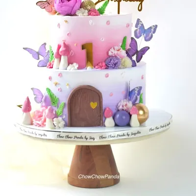 A closer look at the two-tier fairy house cake, showing the details of the edible mushrooms, flowers, and the number '1' for a first birthday.