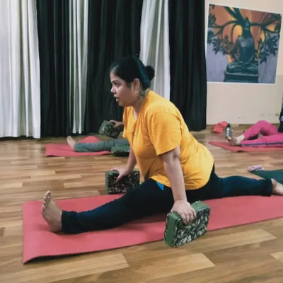 A student works on Hanumanasana (the splits) using yoga blocks for support. Props are essential in yoga therapy to help the body open up gradually and prevent injury.