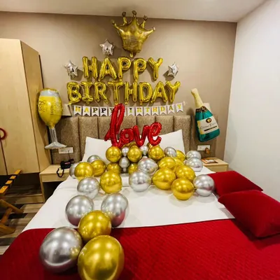 A classic romantic birthday bedroom setup. This decoration includes "Happy Birthday" foil balloons, a foil crown, and gold and silver balloons on the bed.