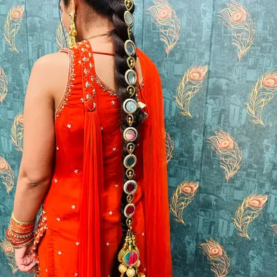 A close-up of a traditional Punjabi parandi (hair accessory) with mirror work and a large golden tassel. This is perfect for adding a folk touch to your Mehendi or Sangeet look.