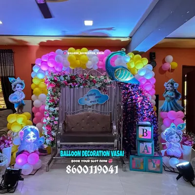 This vibrant baby shower setup features a magnificent peacock next to a decorated jhula. The colorful balloon arch and character cutouts create a lively and festive atmosphere perfect for a home celebration.