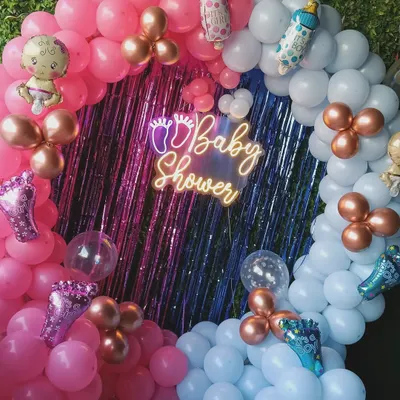 This is a popular baby shower decoration. It features a full ring of pink and blue balloons, a shiny backdrop, a "Baby Shower" neon sign, and cute baby-themed foil balloons.