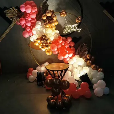A chic birthday ring decoration for a milestone celebration. The setup features a double-ring frame with a cascade of chrome and pastel balloons, accented by a 'Happy Birthday' neon sign for a modern party look.
