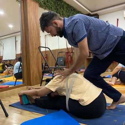 With every exhale, we find a little more space. Here, I'm providing gentle assistance to help a student deepen their forward fold, using a strap to maintain spinal length and blocks to support the feet.