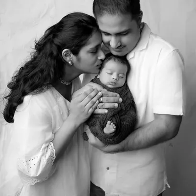 A truly timeless black and white family portrait. The lack of color emphasizes the tender emotions as a mother kisses her newborn, held securely in his father's arms.