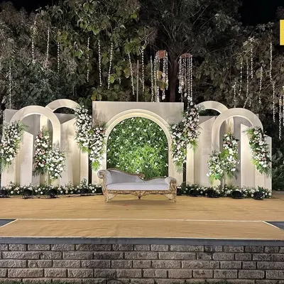 A perfect example of modern elegance. This outdoor stage features a series of clean white arches, a central greenery wall, and asymmetrical floral placements for a look that is both minimal and impactful.