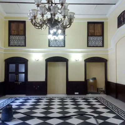 The main hall of a 19th-century haveli after restoration, featuring a classic checkerboard marble floor, restored doors, and a magnificent heritage chandelier, ready for its new life.