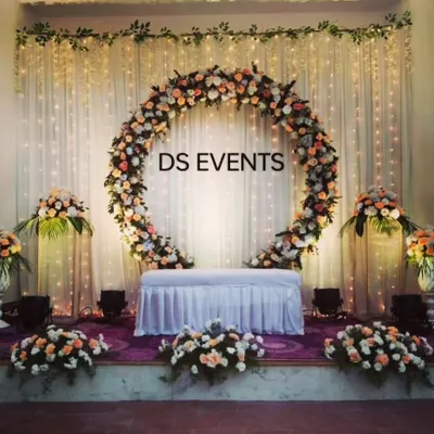 A beautiful and elegant circular floral arch for an indoor reception. This design uses peach and white roses against a backdrop of fairy lights, creating a warm and inviting focal point for the couple's seating.