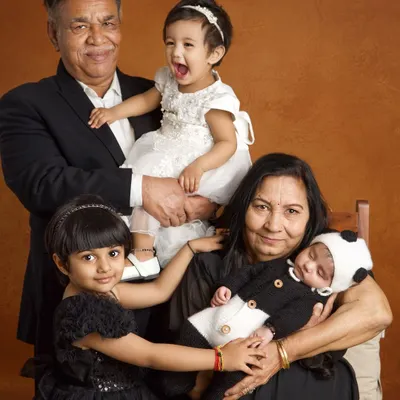 The pure, unscripted joy of three generations together. This portrait captures the grandparents' pride, the siblings' excitement, and the peaceful sleep of the newest family member.