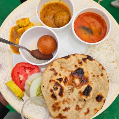 A beautifully plated view of our complete meal thali. It features a freshly made roti, fluffy rice, paneer sabzi, dal, kofta curry, a gulab jamun for dessert, and a side of fresh salad.