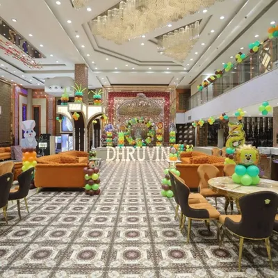 A wide-angle view of a large-scale jungle-themed decoration in a banquet hall. The setup includes a central stage backdrop, marquee letters, and balloon decorations throughout the venue.