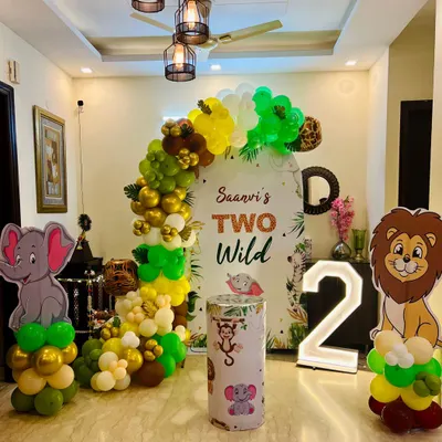 A 'Two Wild' jungle safari theme for a second birthday, set up in a spacious living room. This decor features an arched backdrop, marquee number '2', and cutouts of a lion and elephant.