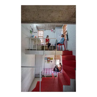 The interior of a room in our 'Stacked Student Housing' project, showing how a split-level design maximizes space. The lofted study area and lower sleeping zone create distinct functional areas within a compact footprint, connected by a bold red steel staircase.