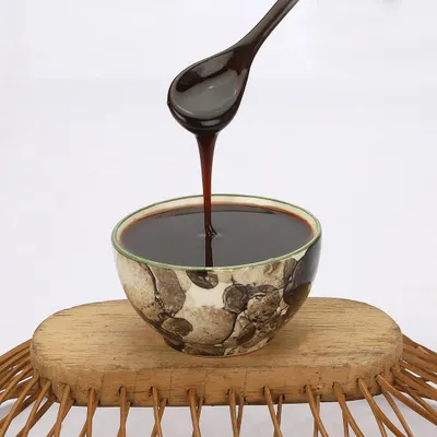A dynamic action shot capturing a thick, dark syrup being poured from a spoon into a bowl. This type of food photography highlights the product's rich texture and viscosity.