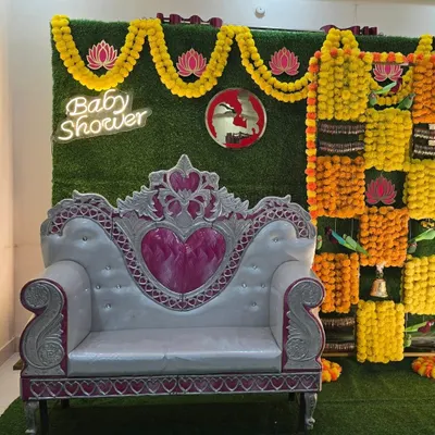 A stunning traditional baby shower backdrop. This design features a checkerboard of yellow and orange marigolds on a grass wall, a modern neon sign, and an elegant throne for the mom-to-be.