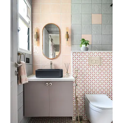 A full view of the pastel bathroom. The combination of pink and grey tiles, along with the patterned floor, creates a playful yet sophisticated look. A modern black sink and brass fixtures add a touch of elegance.