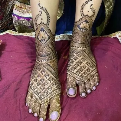 An elegant foot mehendi design featuring a central lotus in a diamond-shaped frame. The pattern extends gracefully up the foot, perfect for showing off with your bridal footwear.