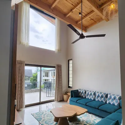 For this beautiful villa in the hills, we designed a living space that feels open and connected to nature. The double height room features a vaulted wooden ceiling, a large teal sectional sofa, and our custom-made wooden coffee table, creating a perfect blend of comfort and rustic charm.