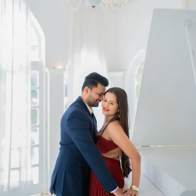 An elegant and romantic pre-wedding photo of Jui and Vaikrant. The all-white room with a grand piano provides a classic and sophisticated backdrop for their portrait.