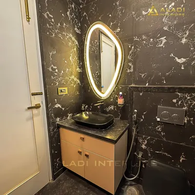A dramatic bathroom design featuring black marble-patterned tiles and a uniquely shaped backlit mirror. The minimalist vanity and black vessel sink add to the modern, luxurious feel.