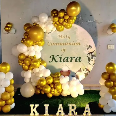 An elegant decoration for a Holy Communion ceremony. This setup features a custom circular backdrop, a white and gold balloon garland, and marquee letters with the child's name.
