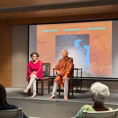 A candid shot of a speaker and presenter on stage during a discussion, with the audience visible.