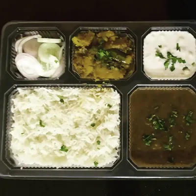 A complete vegetarian thali packed and ready to go. This meal includes dal, a dry vegetable, raita, salad, and rice, offering a balanced and satisfying lunch or dinner.