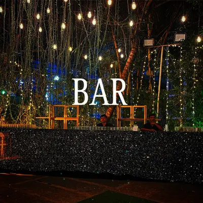A black sequin bar creates a stunning, glamorous look for any evening event. Topped with a bold "BAR" marquee sign and set under a canopy of string lights, this setup is designed to impress.