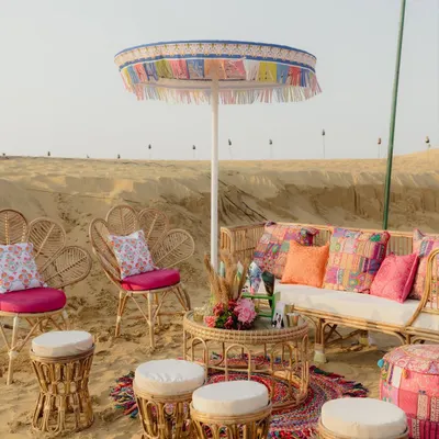 A bohemian Mehendi in the desert. We traded a ballroom for dunes, creating cozy lounge areas with rattan furniture, colorful patchwork cushions, and fringed umbrellas for a relaxed and stylish sundown celebration.