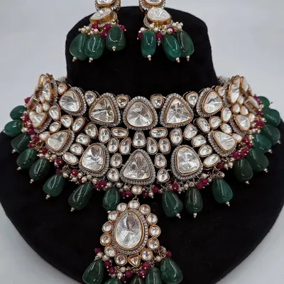 A stunning Polki necklace set with large, uncut triangular stones and emerald green bead drops, displayed on a bust.