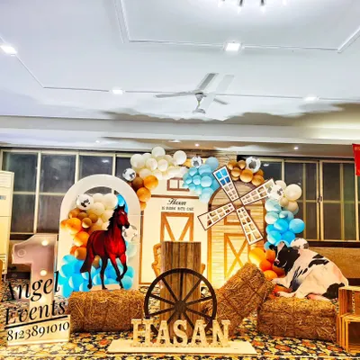 A fun cowboy and farm theme birthday decoration. This setup includes a barn-style backdrop, hay bales, a wooden wagon wheel, and character cutouts of a horse and cow, perfect for a rustic party.
