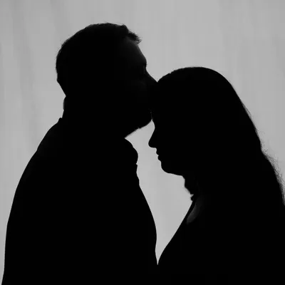 An intimate silhouette of a partner kissing the mom-to-be's forehead. This style creates a timeless and emotional image, focusing purely on the shape and connection.