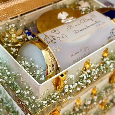 A close-up of a birth announcement hamper for a baby boy. It includes a personalized card that reads "It's a Boy! Dreams do come true," nestled among treats in elegant gold and white packaging.